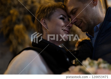 A married couple walks hand-in-hand through the city at night, their faces lit by the soft glow of A married couple walks hand-in-hand through the city at night, their faces lit by the soft glow of 120053471