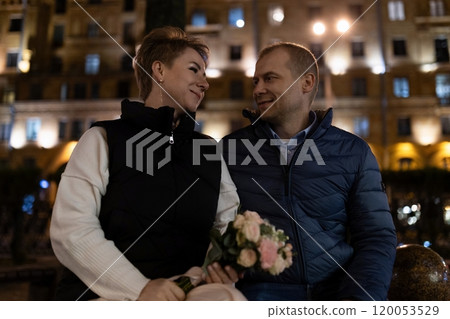 A couple walks through a city at night, the woman holding a bouquet of flowers A couple walks through a city at night, the woman holding a bouquet of flowers 120053529