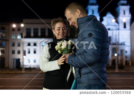 A couple walks through the city at night, the man presenting his wife with a bouquet of flowers A couple walks through the city at night, the man presenting his wife with a bouquet of flowers 120053568