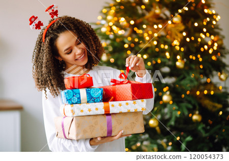 Portrait of young woman in santa claus hat with gift at the Christmas tree. Christmas. New year's. Portrait of young woman in santa claus hat with gift at the Christmas tree. Christmas. New year's. 120054373