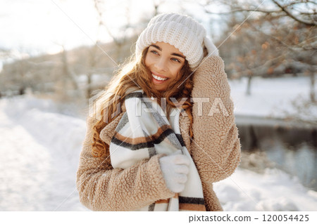 Smiling woman in a scarf and hat is having fun at street holiday fair, drinking hot drink. 120054425
