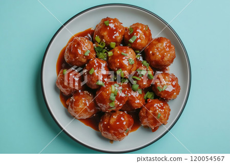 Delicious homemade meatballs coated in a rich sauce, garnished with green onions on a bright blue Delicious homemade meatballs coated in a rich sauce, garnished with green onions on a bright blue 120054567