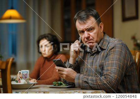 Tense dinner conversation between a couple in a cozy kitchen as a smartphone rings unexpectedly late 120054848