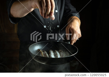 In a dimly lit kitchen, a chef expertly sprinkles salt over fresh shrimp in a hot pan, creating an inviting atmosphere filled with anticipation of delicious flavors 120055025