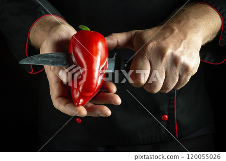 With deft hands, a chef holds a vibrant red pepper while expertly slicing it with a sharp knife, showcasing culinary precision in a dramatic, low-light setting With deft hands, a chef holds a vibrant red pepper while expertly slicing it with a sharp knife, showcasing culinary precision in a dramatic, low-light setting 120055026