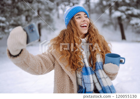 Portrait of a beautiful woman in warm clothes takes selfie with a hot drink from a thermos in hands. Portrait of a beautiful woman in warm clothes takes selfie with a hot drink from a thermos in hands. 120055130