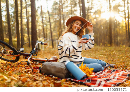 Relax in forest Woman sits on blanket, drinks from thermos, enjoys autumn atmosphere in sunny forest 120055571