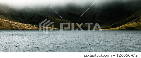 A misty lake surrounded by lush hills in a remote mountainous area in the early hours of the morning. 120056472