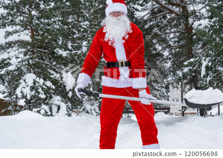 Santa Claus cleans snow with shovel in winter outdoors after a snowfall. Cleaning the streets in the village, clearing the passage for cars, difficult weather conditions for Christmas and New Year Santa Claus cleans snow with shovel in winter outdoors after a snowfall. Cleaning the streets in the village, clearing the passage for cars, difficult weather conditions for Christmas and New Year 120056698
