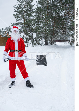 Santa Claus cleans snow with shovel in winter outdoors after a snowfall. Cleaning the streets in the village, clearing the passage for cars, difficult weather conditions for Christmas and New Year Santa Claus cleans snow with shovel in winter outdoors after a snowfall. Cleaning the streets in the village, clearing the passage for cars, difficult weather conditions for Christmas and New Year 120056708