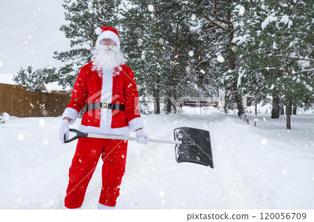 Santa Claus cleans snow with shovel in winter outdoors after a snowfall. Cleaning the streets in the village, clearing the passage for cars, difficult weather conditions for Christmas and New Year Santa Claus cleans snow with shovel in winter outdoors after a snowfall. Cleaning the streets in the village, clearing the passage for cars, difficult weather conditions for Christmas and New Year 120056709
