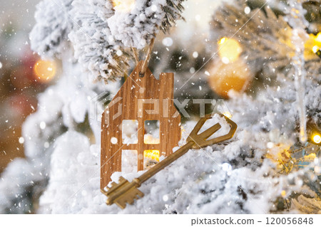 Key and tiny house keychain in hand on background fairy lights Christmas tree. gift for New Year, Christmas. Building, design, project, moving, insurance, mortgage, rent and purchase real estate. 120056848
