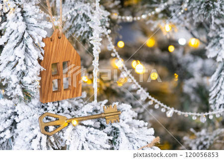 Key and tiny house keychain in hand on background fairy lights Christmas tree. gift for New Year, Christmas. Building, design, project, moving, insurance, mortgage, rent and purchase real estate. 120056853