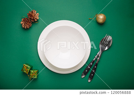 Christmas table setting featuring empty plate, cutlery, festive decorations on green background 120056888