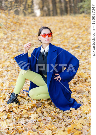 Beautiful young woman enjoying autumn day in nature, walking down the forest path covered with colorful fallen leaves and relaxing 120057347