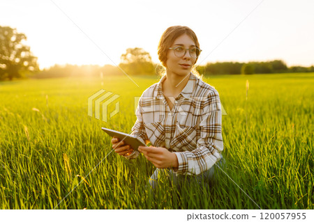 Experienced woman farmer with digital tablet in hands on green wheat field. Concept of gardening. 120057955