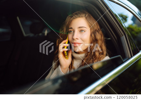 Positive young woman in casual clothes sits in the back seat of a car with a mobile phone. Positive young woman in casual clothes sits in the back seat of a car with a mobile phone. 120058025