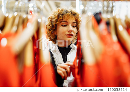 young attractive red-haired woman choosing red clothes in boutique 120058214