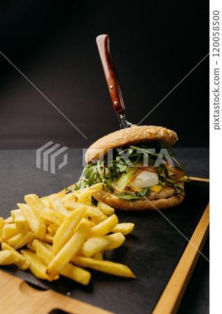 Gourmet burger with arugula, egg, and fresh vegetables served with crispy golden fries on board 120058500