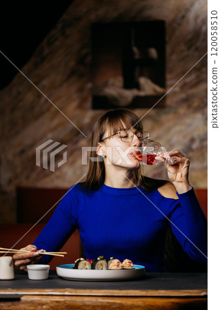 Woman enjoying sushi and sipping rose wine in a relaxed, elegant restaurant setting Woman enjoying sushi and sipping rose wine in a relaxed, elegant restaurant setting 120058510