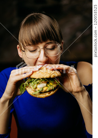 Woman enjoying a big bite of a gourmet burger with fresh greens, savoring each delicious flavor 120058525
