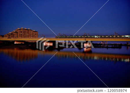 Noborito: Odakyu Line trains shining in the setting sun as seen from upstream the Tama River bank 120058974