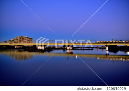 Noborito: Odakyu Line trains shining in the setting sun as seen from upstream the Tama River bank 120059029