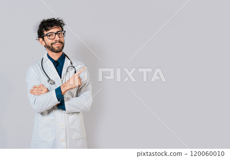 Smiling doctor pointing finger isolated. Doctor pointing at an isolated white space. Young doctor pointing finger at a blank space Smiling doctor pointing finger isolated. Doctor pointing at an isolated white space. Young doctor pointing finger at a blank space 120060010