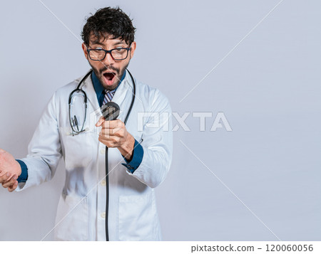 Surprised young doctor with blood pressure monitor. Surprised doctor looking at tensiometer isolated Surprised young doctor with blood pressure monitor. Surprised doctor looking at tensiometer isolated 120060056