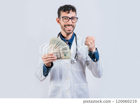 Smiling young doctor holding money isolated. Cheerful doctor holding dollars bills isolated 120060219