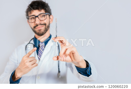 Handsome doctor holding and pointing a syringe isolated. Smiling doctor showing a syringe on isolated background. Doctor and vaccine concept Handsome doctor holding and pointing a syringe isolated. Smiling doctor showing a syringe on isolated background. Doctor and vaccine concept 120060220