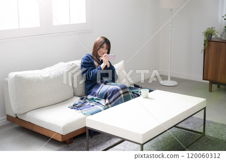 Young woman using smartphone on sofa, smiling and looking at smartphone, happy and joyful expression, autumn and winter, wide-angle full-body aerial view Young woman using smartphone on sofa, smiling and looking at smartphone, happy and joyful expression, autumn and winter, wide-angle full-body aerial view 120060312