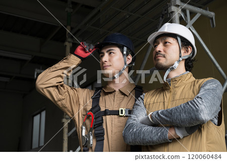 兩名高空作業人員和繫著安全帶的戶外工作人員抬頭仰望，表情嚴肅嚴肅。 120060484