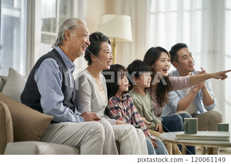 three generation asian family watching tv together at home 120061149