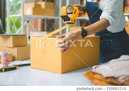 Startup small business owners holding packing machine and sealing cardboard boxes with tape to deliver products to customers- concept shopping online Startup small business owners holding packing machine and sealing cardboard boxes with tape to deliver products to customers- concept shopping online 120061219