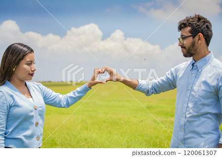 Happy couple making a heart shape with their hands, couple in love in the field making a heart shape with hands, beautiful couple in the field making a heart shape with hands 120061307