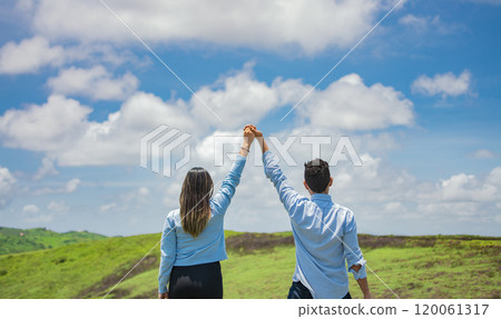 Back view of couple on the hill with hands raised to the sky, Happy couple in the field raising hands to the sky, Concept of a happy and free couple in the field 120061317