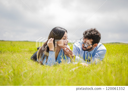 A couple lying on the grass looking at each other, young couple in love lying on the grass touching each other's faces, two people in love lying on the grass looking at each other 120061332
