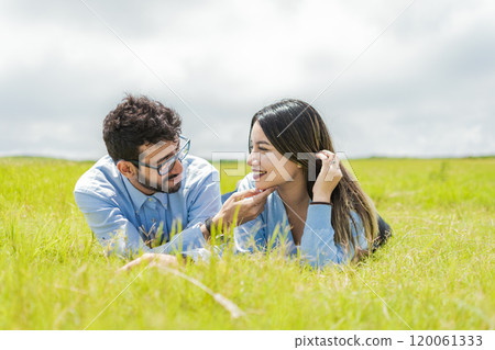 Young couple in love lying on the grass touching each other's faces, two people in love lying on the grass looking at each other, A couple lying on the grass looking at each other 120061333