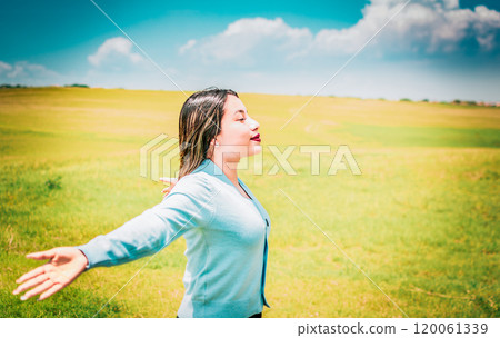 Happy girl spreading arms breathing fresh air in the field. Relaxed woman breathing fresh air in a beautiful field on a sunny day 120061339