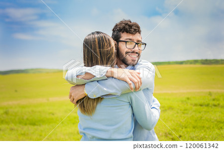 A man hugging his woman in a beautiful field, Close up of a happy couple hugging in the field, a young couple in love hugging in the green field 120061342