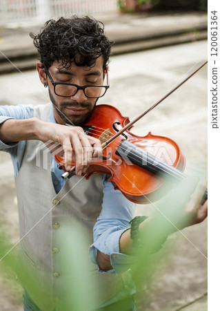 Handsome man in vest playing violin outdoors. Close up of violinist man playing a melody outdoors. Violinist artist playing a melody outdoors. 120061364