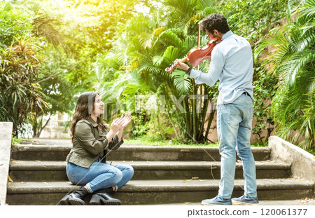 Violinist man playing a melody to a girl sitting on the stairs. Man playing violin for girl sitting on stairs outside. Concept of man playing violin to people on the street Violinist man playing a melody to a girl sitting on the stairs. Man playing violin for girl sitting on stairs outside. Concept of man playing violin to people on the street 120061377