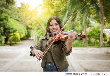 Young woman playing the violin outdoors. Portrait of a girl playing the violin outdoors, Close up of a girl with her violin playing a melody outdoors, Concept of smiling female violinist 120061378