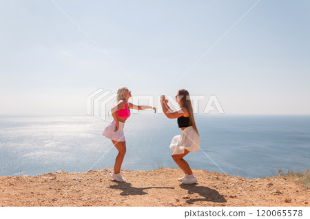Two women are standing on a beach, one in a pink top 120065578