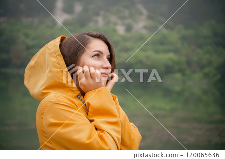A woman in a yellow raincoat is standing in the rain A woman in a yellow raincoat is standing in the rain 120065636