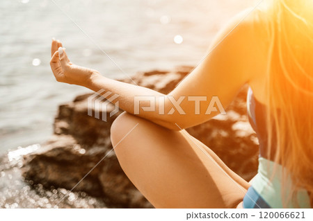 Yoga on the beach. A happy woman meditating in a yoga pose on the beach, surrounded by the ocean and rock mountains, promoting a healthy lifestyle outdoors in nature, and inspiring fitness concept. 120066621