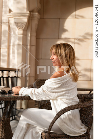 Woman, Patio, Relaxation - Woman in white sits at table on a sunny patio, enjoying the outdoors. 120066641