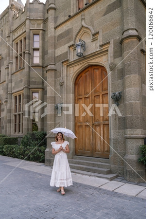 Woman, Umbrella, Castle. A woman in a white dress holds an umbrella while standing in front of a stone castle. 120066642