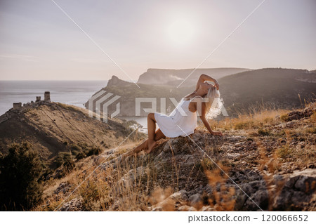 A woman is sitting on a hillside overlooking the ocean. She is wearing a white dress and has blonde hair. The scene is serene and peaceful, with the ocean in the background. A woman is sitting on a hillside overlooking the ocean. She is wearing a white dress and has blonde hair. The scene is serene and peaceful, with the ocean in the background. 120066652